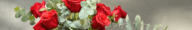 Elegant bouquet of red roses with eucalyptus leaves on a wooden stand, perfect for any occasion.