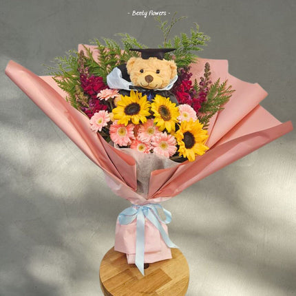 Teddy Bright bouquet featuring sunflowers, pink flowers, and a graduation teddy bear in a joyful arrangement.