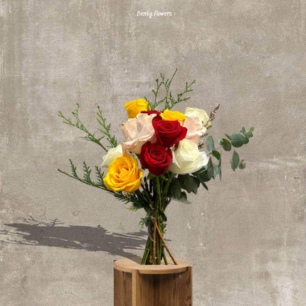 Colorful bouquet featuring red, yellow, and white roses with greenery in a wooden vase.