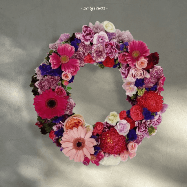 Vibrant floral wreath arrangement featuring pink and purple gerbera daisies for sympathy and memorial services.