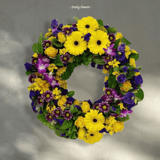 Bright funeral wreath featuring yellow gerbera daisies, purple roses, and varied flowers for sympathy in Melbourne.