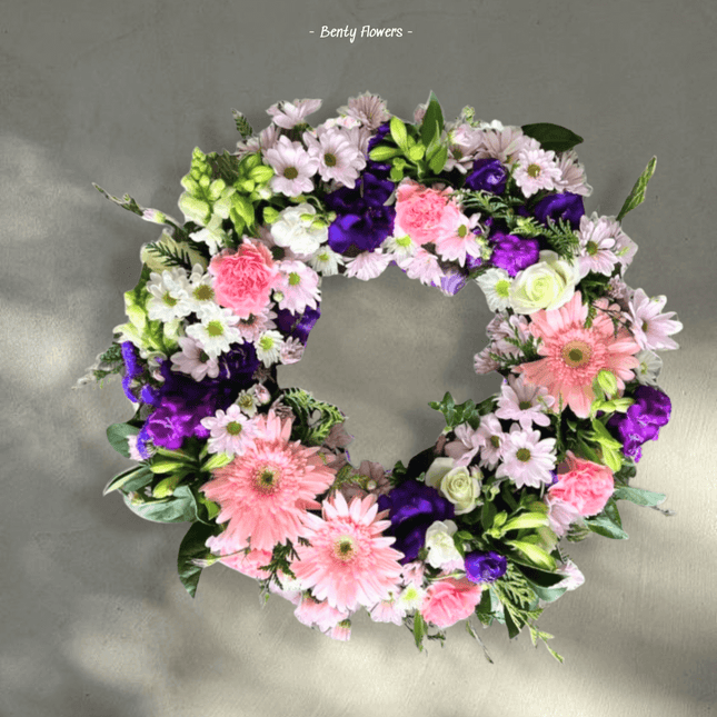 Calm Halo funeral flower wreath featuring pink gerbera daisies, purple lisianthus, and white chrysanthemums.