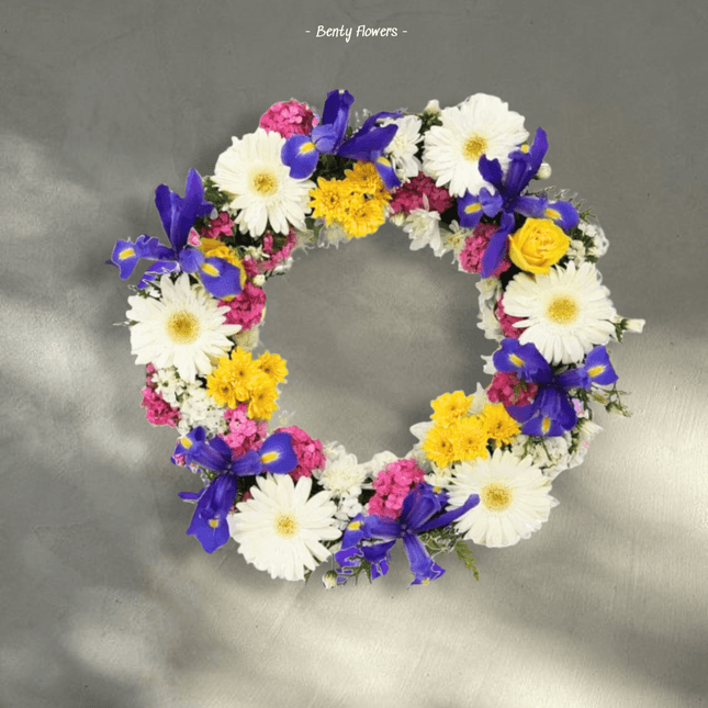 Vibrant Colourful Tribute wreath featuring white daisies, pink blossoms, and yellow and blue flowers, symbolizing remembrance.