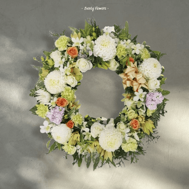 Peaceful Light funeral wreath featuring white blooms, soft greenery, and orange accents for sympathy and remembrance.