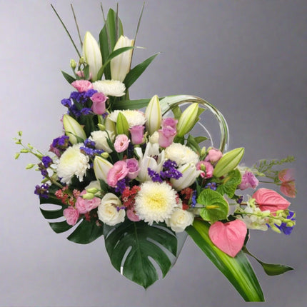 Elegant Grace arrangement with white lilies, white chrysanthemums, pink anthuriums, pink lisianthus, purple statice, and lush greenery.