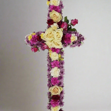 Heavenly Grace cross floral arrangement with white roses, red roses, pink carnations, purple chrysanthemums, and lush greenery.