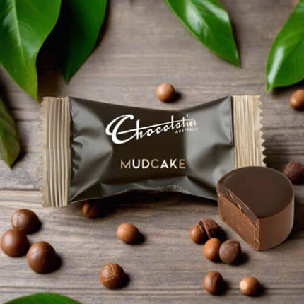 Chocolatier Australia Mudcake chocolate on a wooden surface with cocoa beans and green leaves.