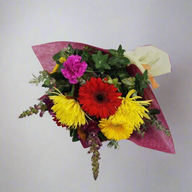 Vibrant Sunshine Bouquet featuring red gerbera daisies, yellow chrysanthemums, pink carnations, and lush greenery, elegantly wrapped in red and orange paper.