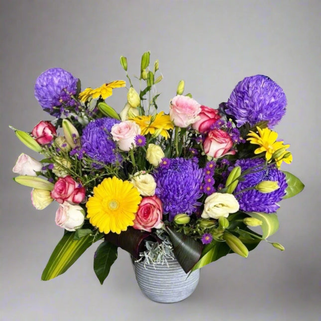 Vibrant Harmony – Mixed Floral Arrangement with purple asters, yellow gerberas, mixed roses, and lush greenery.