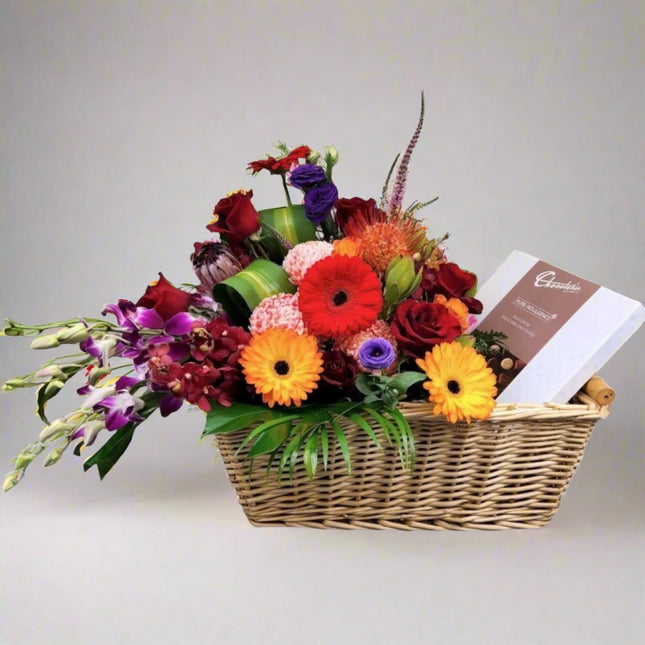 Celebration Bliss – Colorful Gift Basket with gerberas, roses, orchids, and gourmet chocolates.