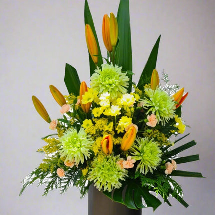 Golden Radiance vase arrangement with orange lilies, green chrysanthemums, yellow solidago, peach carnations, and lush greenery.