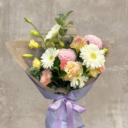 Beautiful pastel flower bouquet featuring white daisies, pink chrysanthemums, and yellow roses with a purple ribbon.