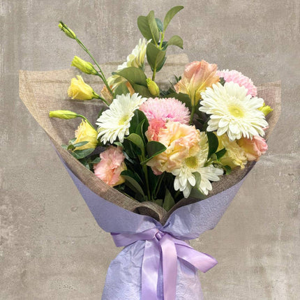 Elegant arrangement of pastel flowers with white daisies, pink chrysanthemums, and yellow roses, tied with a purple ribbon.