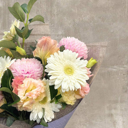 Charming bouquet of pastel flowers including white daisies, pink chrysanthemums, and yellow roses in a burlap wrap.