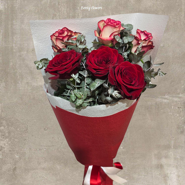 Elegant bouquet of deep red and pink-tipped roses, wrapped in red and white paper with a satin ribbon. Accented with lush green foliage, this floral arrangement is perfect for romantic gifts and special occasions – Betty Flowers.