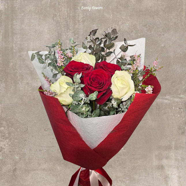 A beautifully arranged bouquet featuring deep red and soft ivory roses, complemented by delicate pink floral accents and lush green eucalyptus leaves. The bouquet is elegantly wrapped in red and white paper, tied with a satin ribbon, creating a sophisticated and romantic presentation. Perfect for expressing love and appreciation.