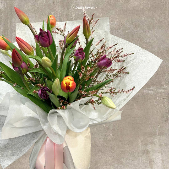 A bouquet of vibrant tulips wrapped in white paper with a pink ribbon.