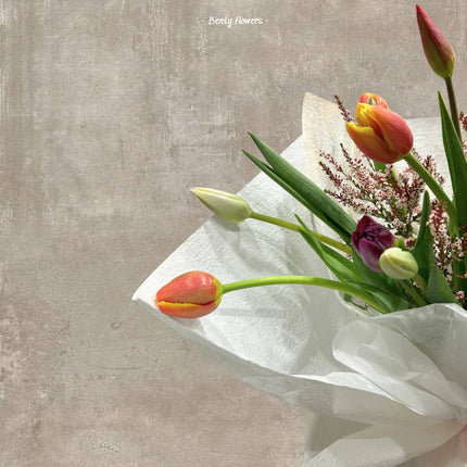 A colorful tulip bouquet wrapped in white paper, showcasing the vibrant hues of the flowers.