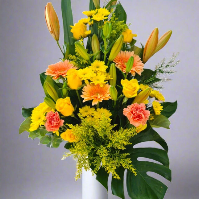 Golden Sunrise vase arrangement with orange lilies, yellow roses, peach carnations, yellow chrysanthemums, and lush greenery.