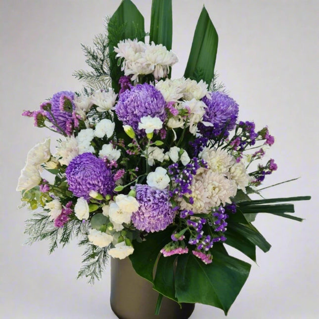 Violet Serenity vase arrangement with purple chrysanthemums, white chrysanthemums, white carnations, purple statice, and lush greenery.