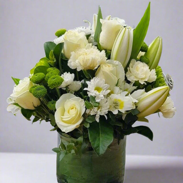 Peaceful Bliss vase arrangement with white roses, white lilies, white carnations, green button mums, and lush greenery.