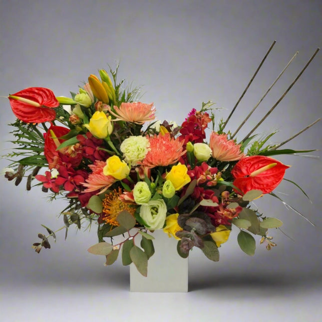 Sunset Splendor – Vibrant Floral Arrangement with red anthuriums, yellow roses, and exotic orchids.