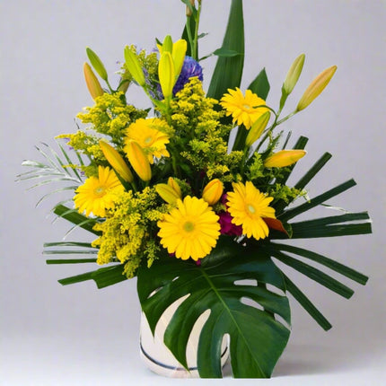 Sunny Joy vase arrangement with yellow gerberas, yellow lilies, yellow solidago, purple statice, and lush greenery