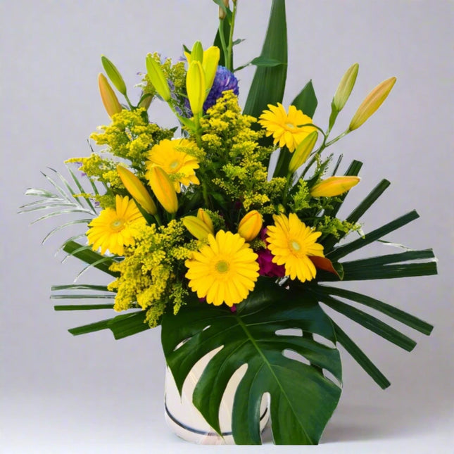 Sunny Joy vase arrangement with yellow gerberas, yellow lilies, yellow solidago, purple statice, and lush greenery