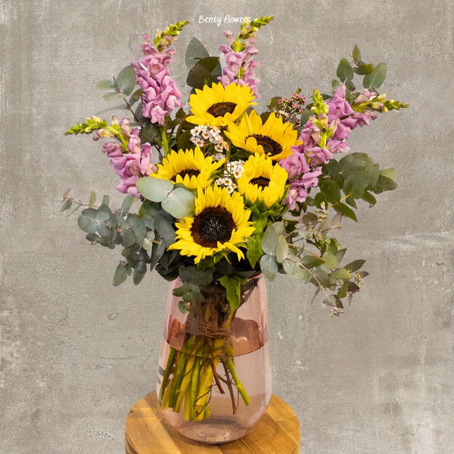 Bright Sunshine Mix bouquet with sunflowers and pink snapdragons in elegant glass vase, perfect for any occasion.