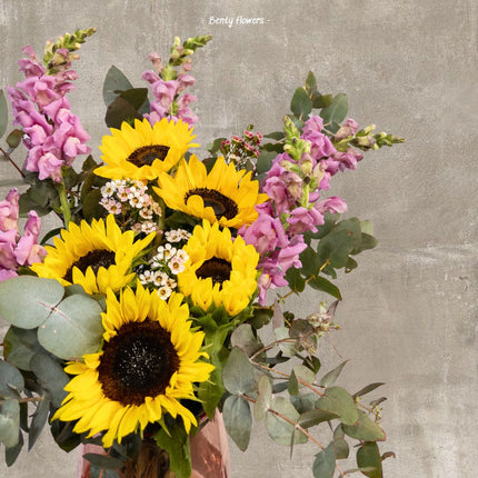 Daily Bloom Bouquet featuring vibrant sunflowers, snapdragons, eucalyptus, and wax flowers elegantly wrapped in paper, perfect for any occasion.