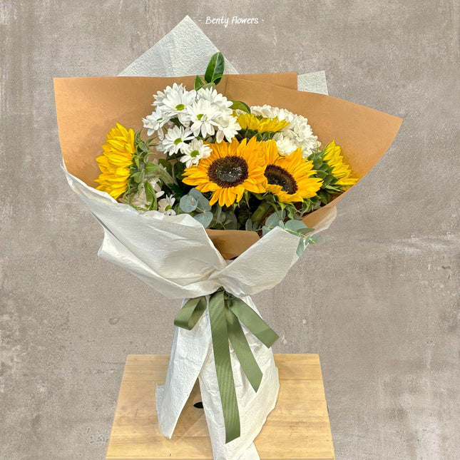 Elegant sunflower bouquet with fresh greenery, wrapped in premium beige and white paper, tied with a green ribbon, perfect for celebrations or gifting.